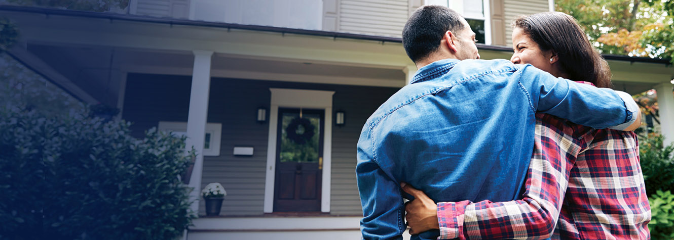 Couple hugging and looking at each other in front of home.