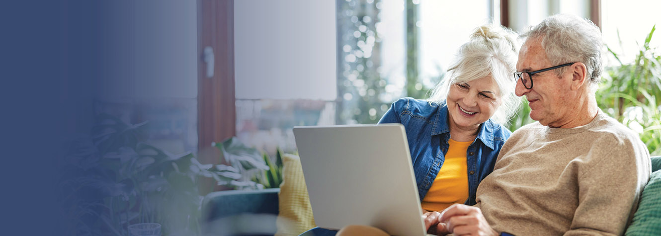 Happy couple sitting on couch looking at computer screen together.