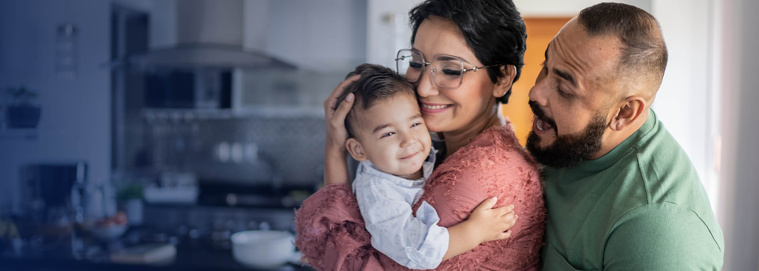 Mother holding smiling son while father makes silly face.