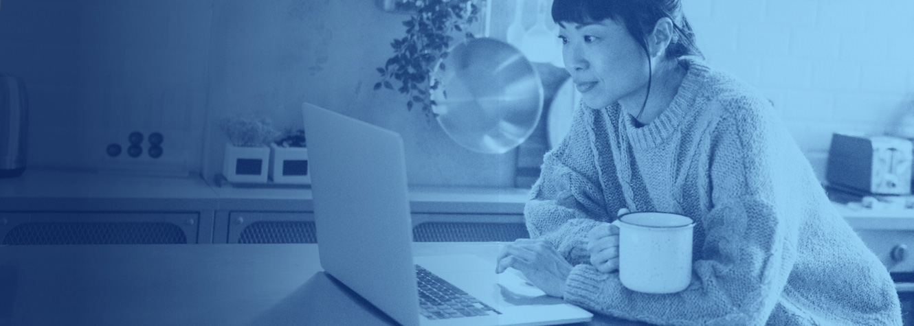 Woman enjoying a hot drink while looking at her laptop