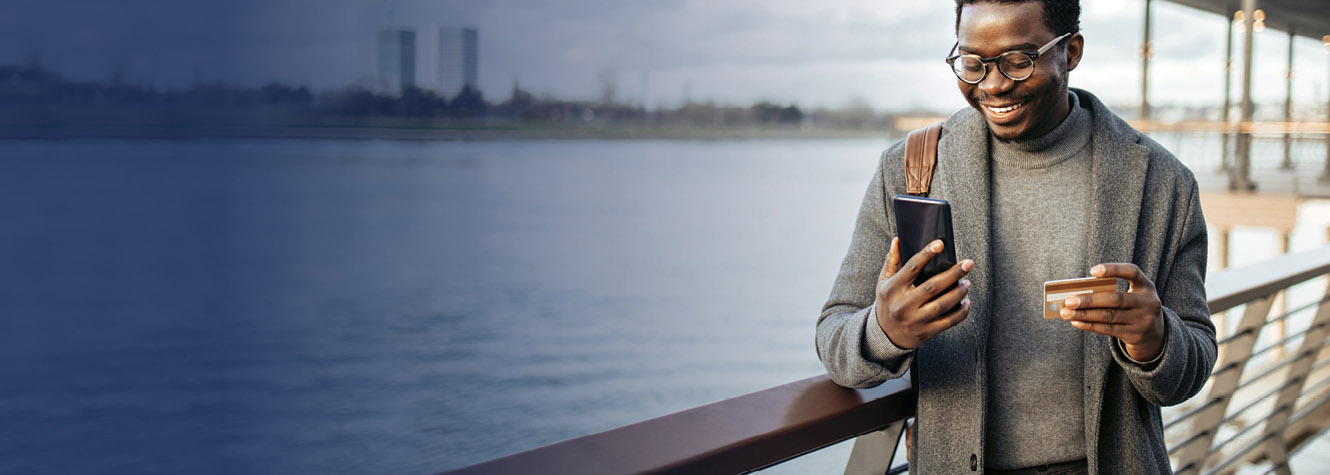 Person standing by waterfront, holding phone and bank card.